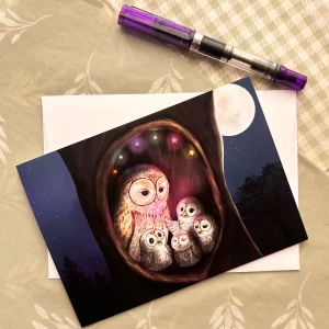 Tracy Serafini owl family greeting card laid flat with envelope and fountain pen, featuring mother owl and owlets in a moonlit tree hollow
