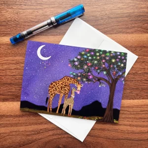 Giraffe mother and baby night sky greeting card by Tracy Serafini displayed on a wood desk with white envelope