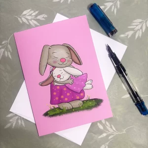 Tom Serafini mother and daughter bunny greeting card laid flat with envelope and pen, mama bunny cradling her little girl in a purple polka dot dress